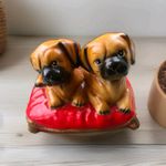 Pair of vintage pottery figurines depicting pug puppies sitting on a red cushion